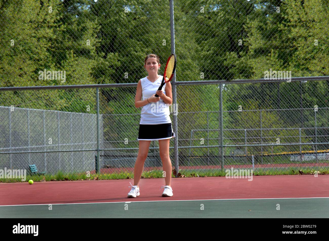 Varsity tennis player waits to receive the serve during a tennis match.  She is wearing a tennis skirt and tee shirt.  The court is outdoors. Stock Photo