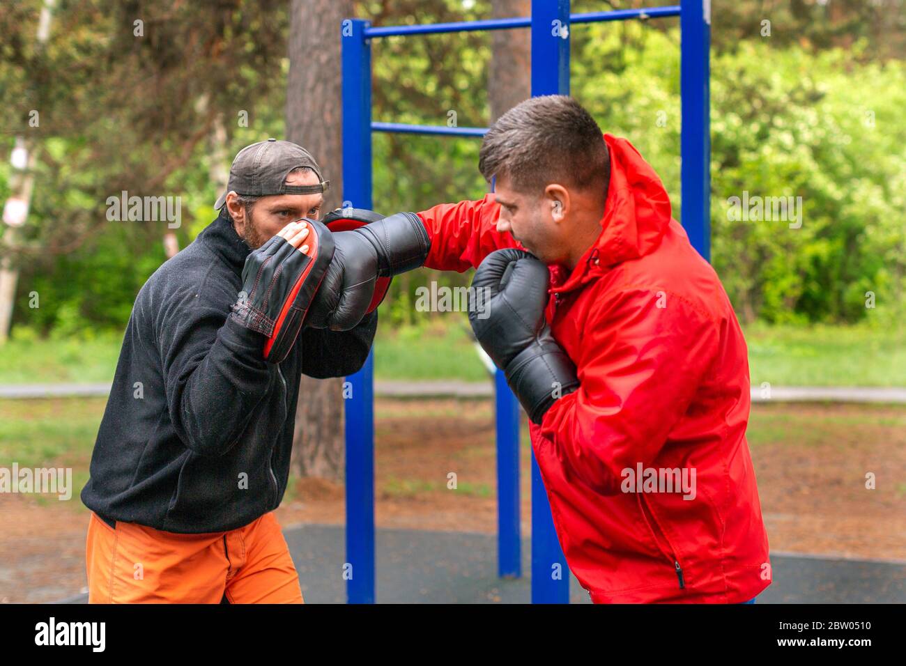Middleaged boxer training with coach outdoors. Boxing paws work. Healthy lifestyle concept