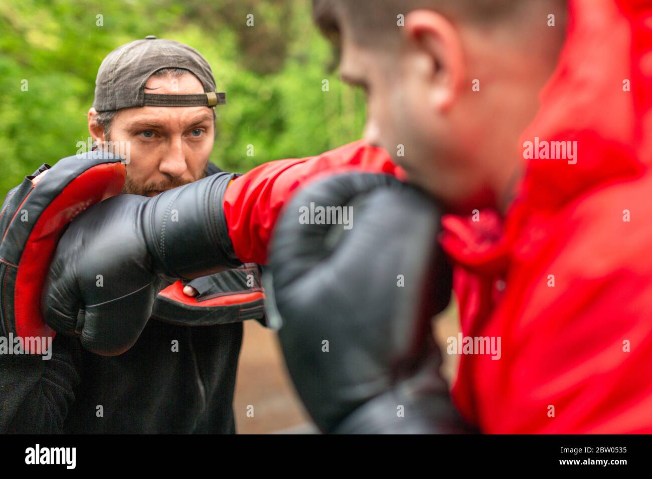 Middleaged boxer training with coach outdoors. Healthy lifestyle concept. Boxing paws workout