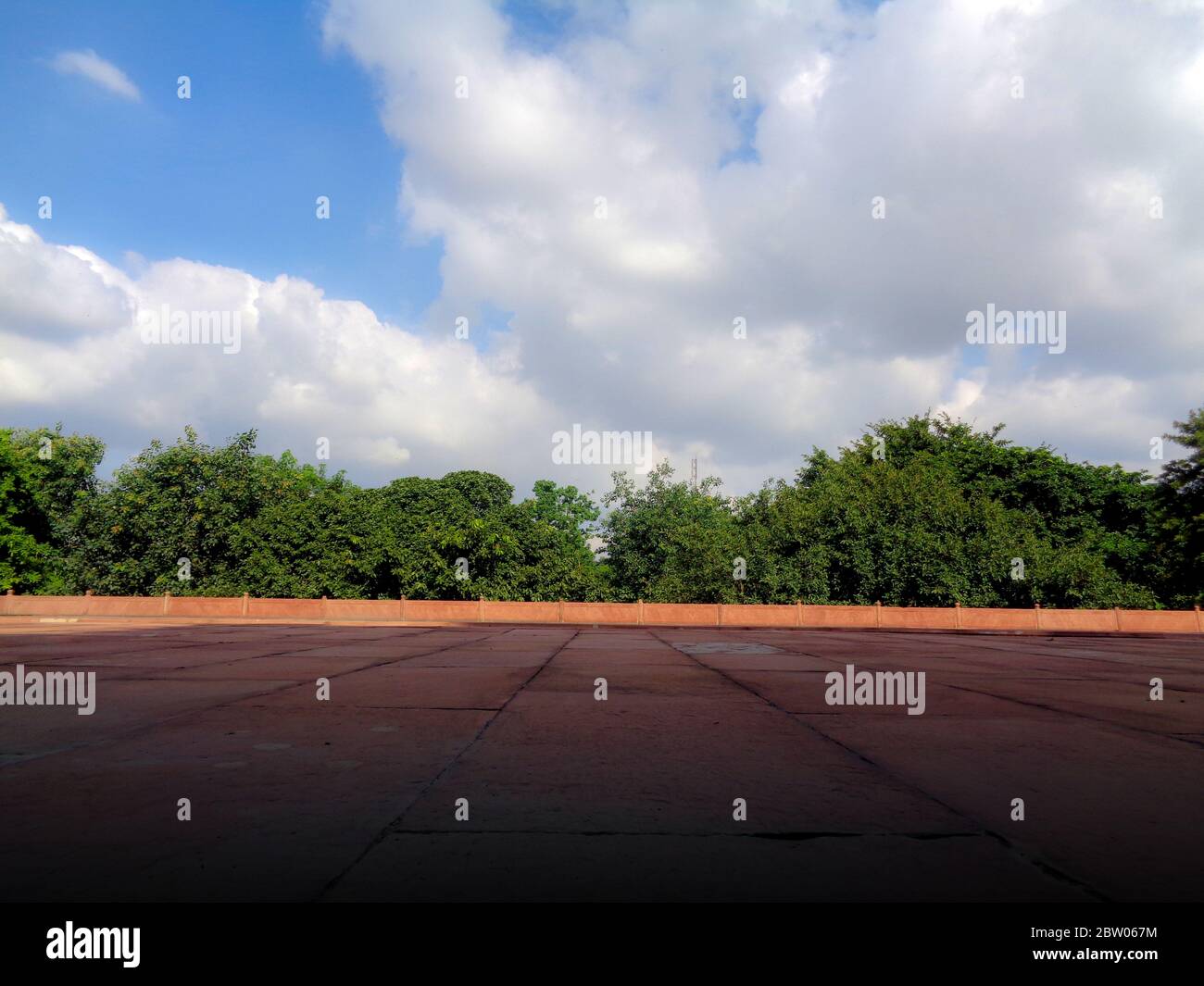 Blue dramatic cloudy sky trees and red marble floor Stock Photo