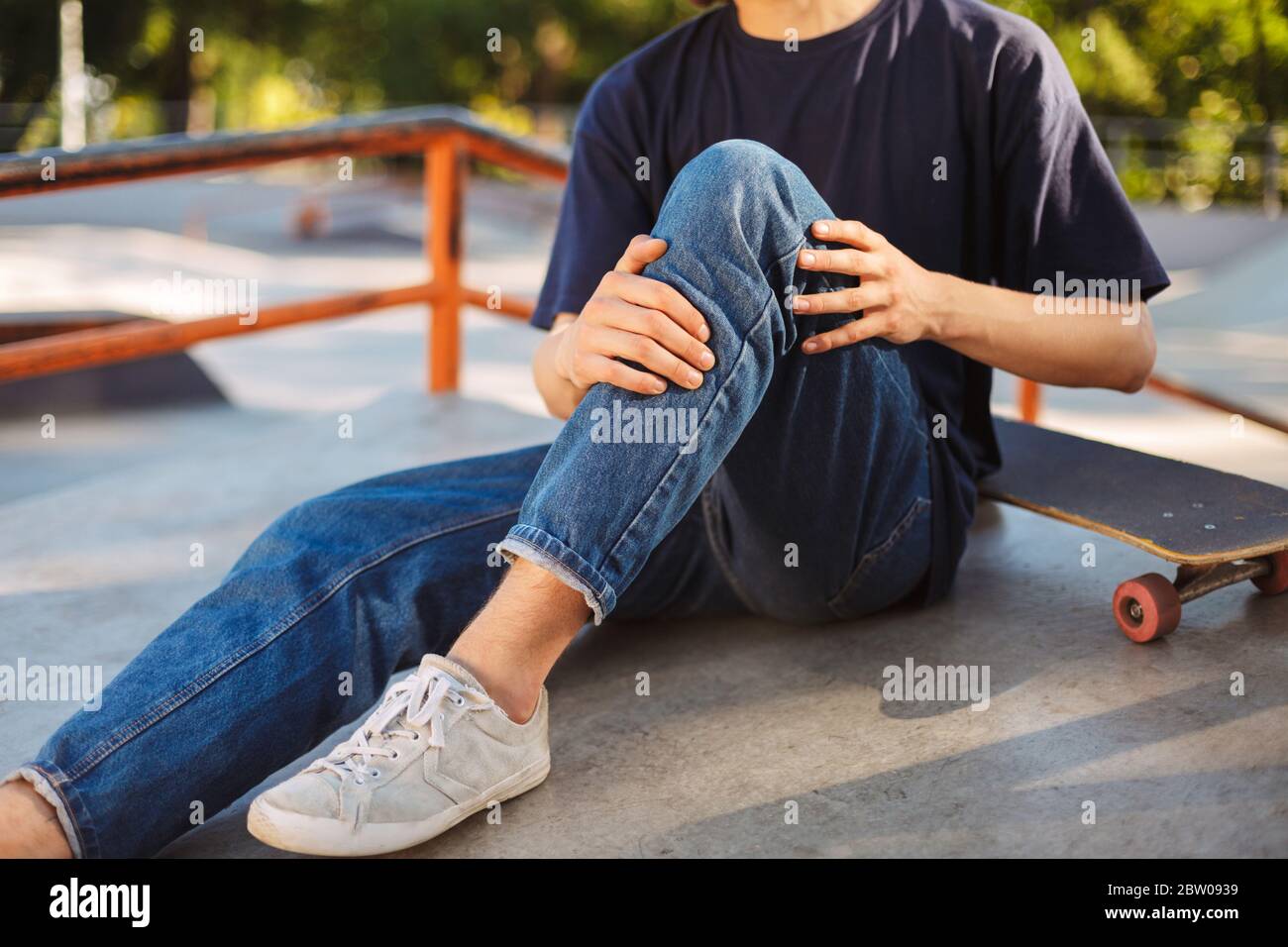 Close up skater holding his painful leg with skateboard near at