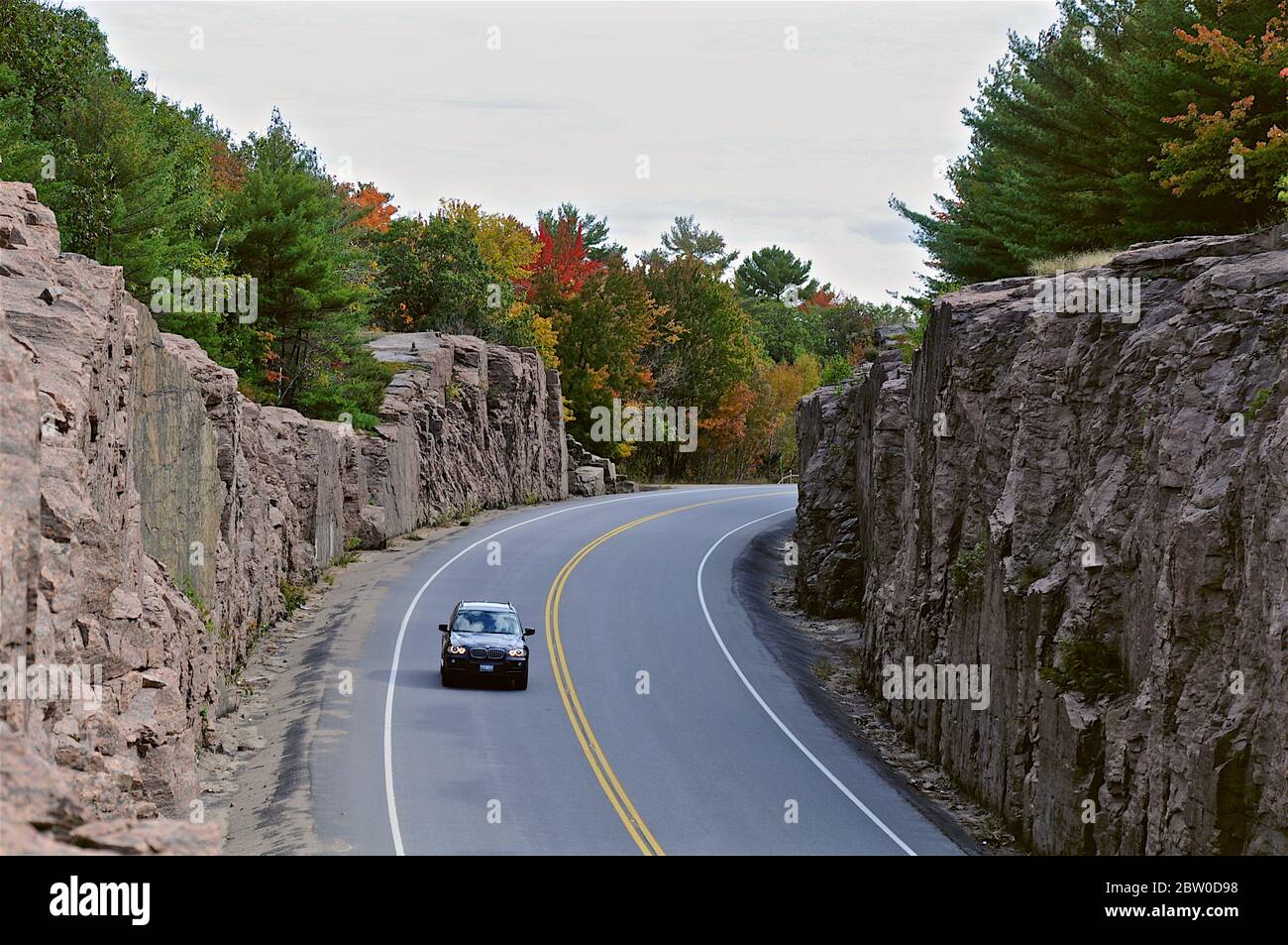 Milford Bay, Ontario / Canada - 10/05/2008: Mountain road cut through the pink granite. Landscape with rocks, autumn leaf color, and beautiful asphalt Stock Photo
