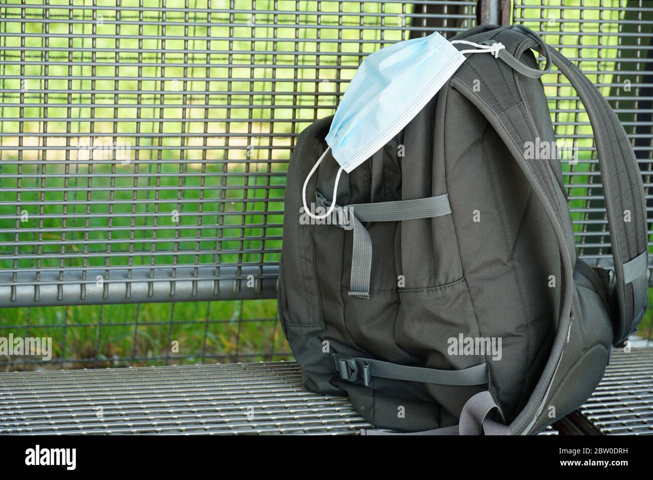 A backpack with a N95 facial mask attached on it on a metal bank of a train station during Lockdown due to coronavirus, covid-19 with its lockdown Stock Photo
