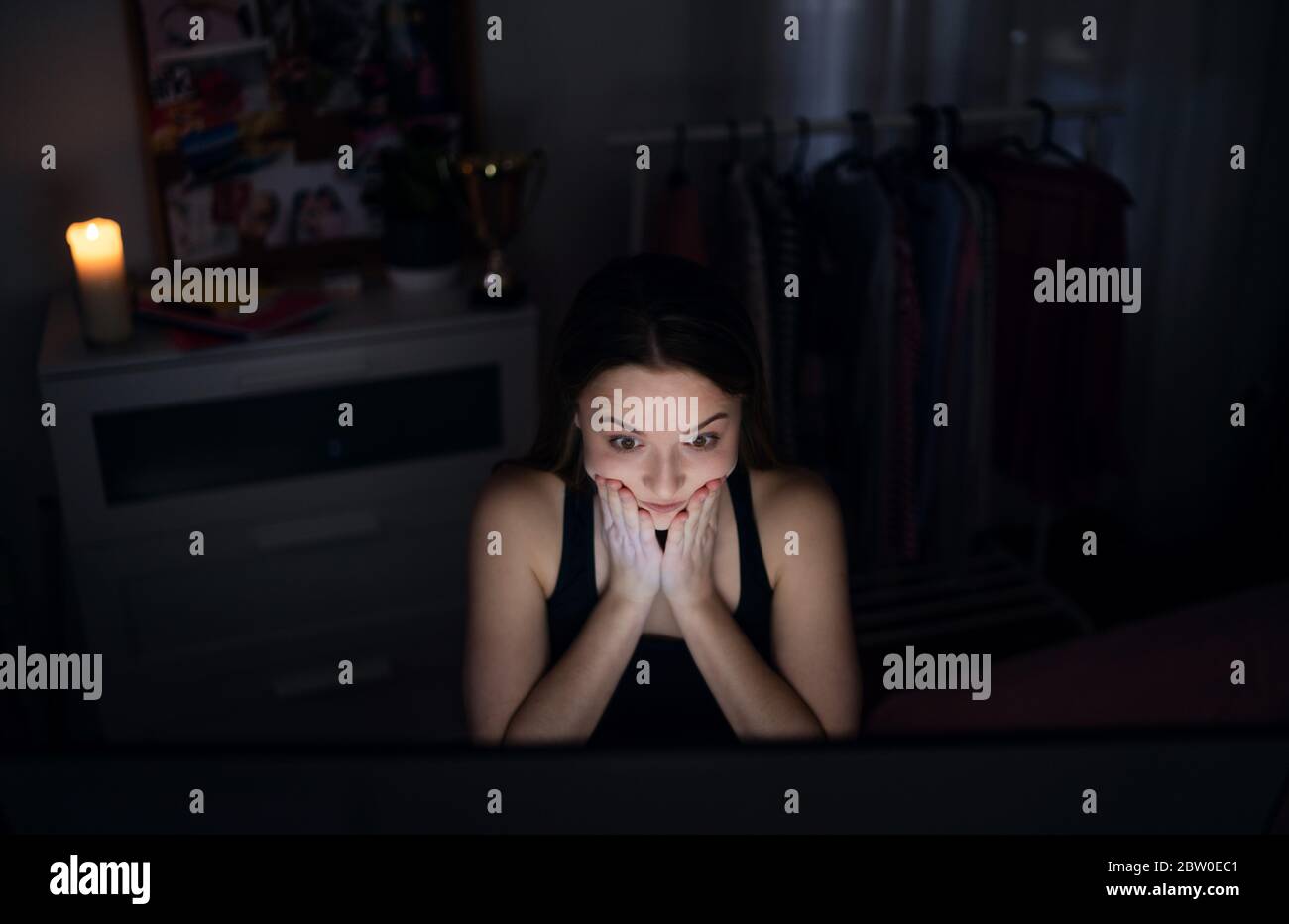Scared and worried young girl with laptop sitting indoors, internet abuse concept. Stock Photo