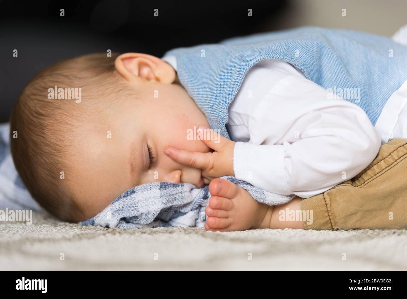Little baby boy fell asleep on the floor in bent position with toes near face, sucking fingers