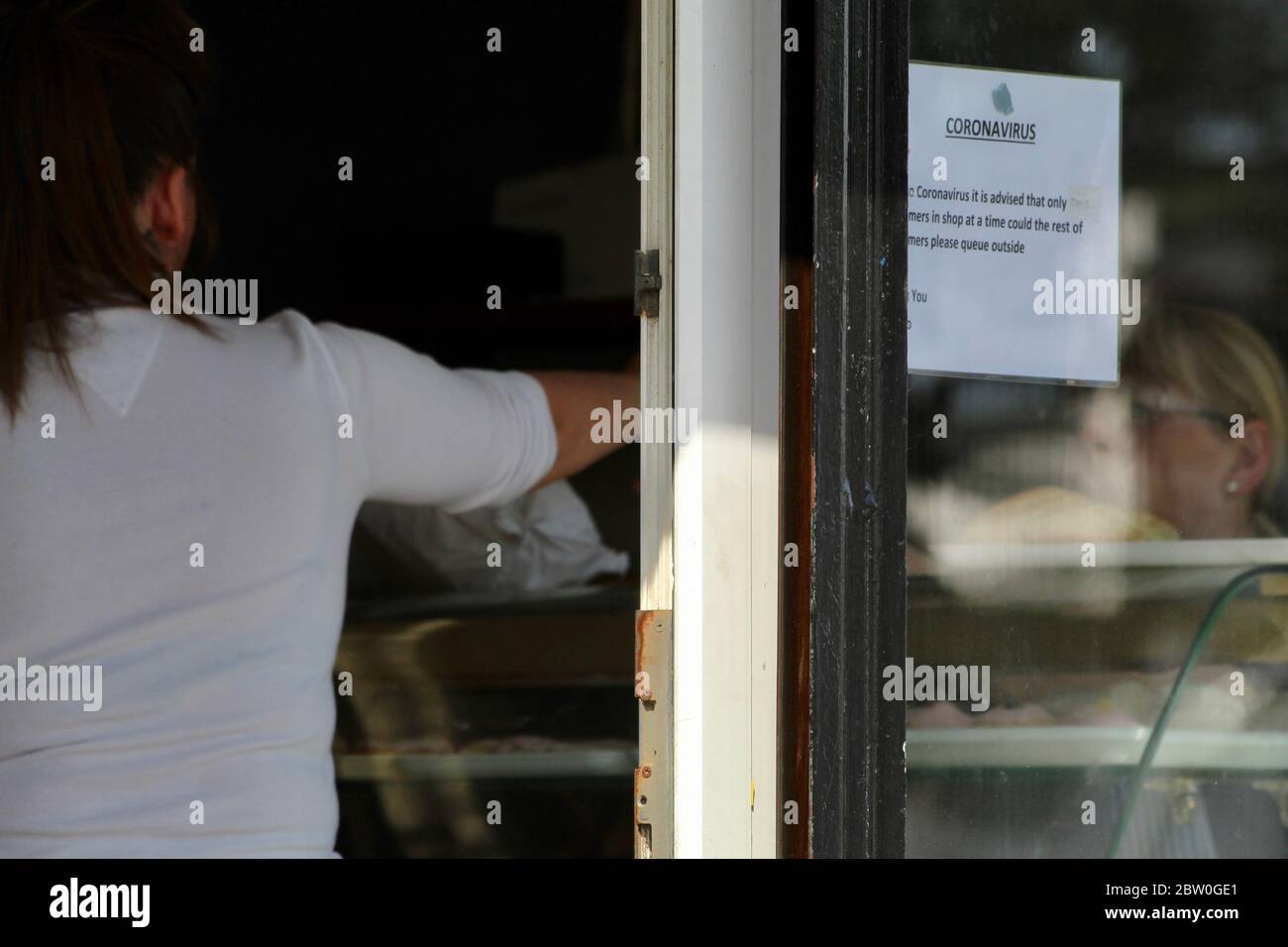 customer paying for bread and sales person at a small bakery with coronavirus notice on the window Stock Photo