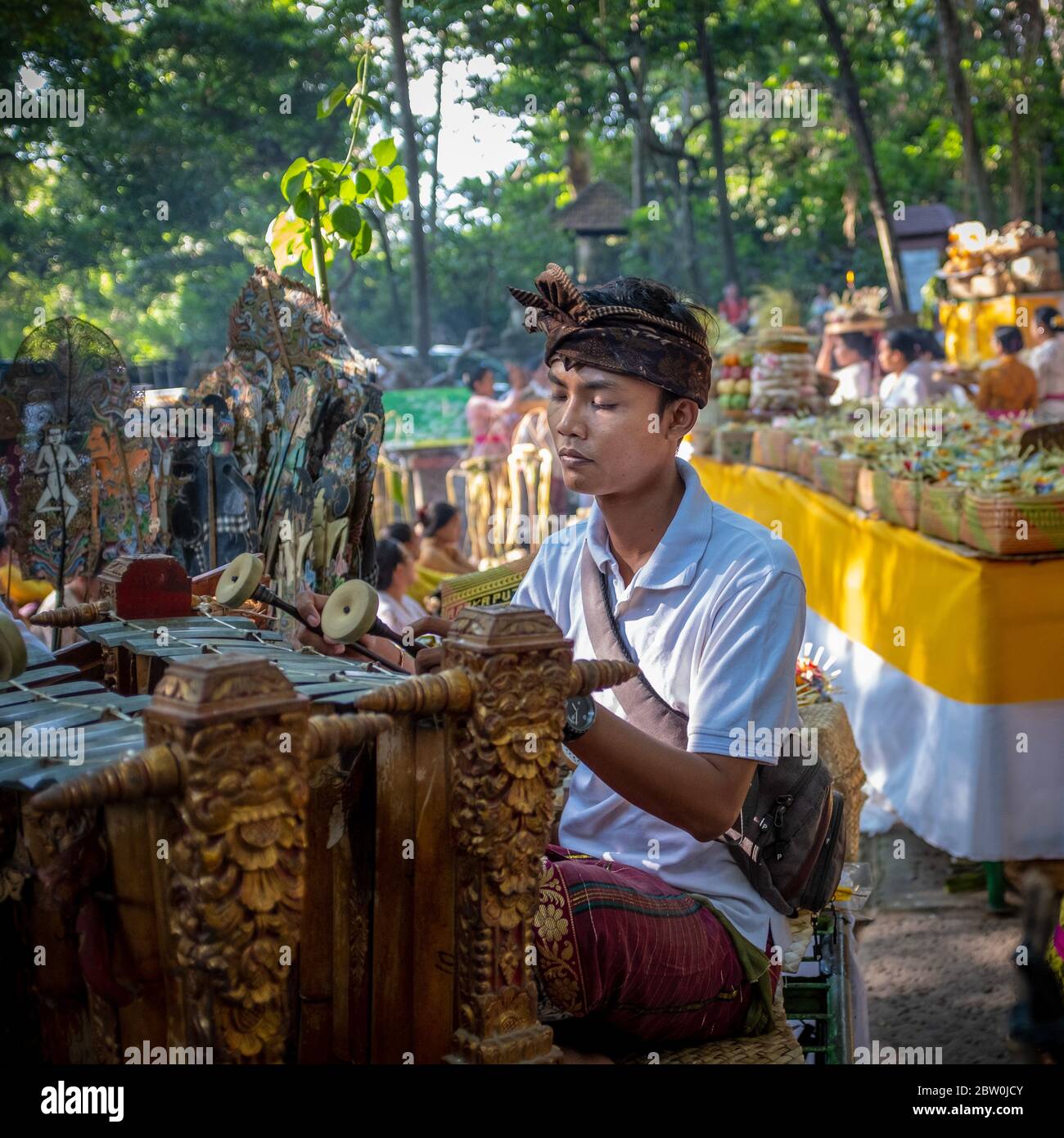 Ubud, Bali, Indonesia - May 5, 2018: Young traditional musical instrument man player, wearing traditional clothing with an ongoing ceremony in the bac Stock Photo
