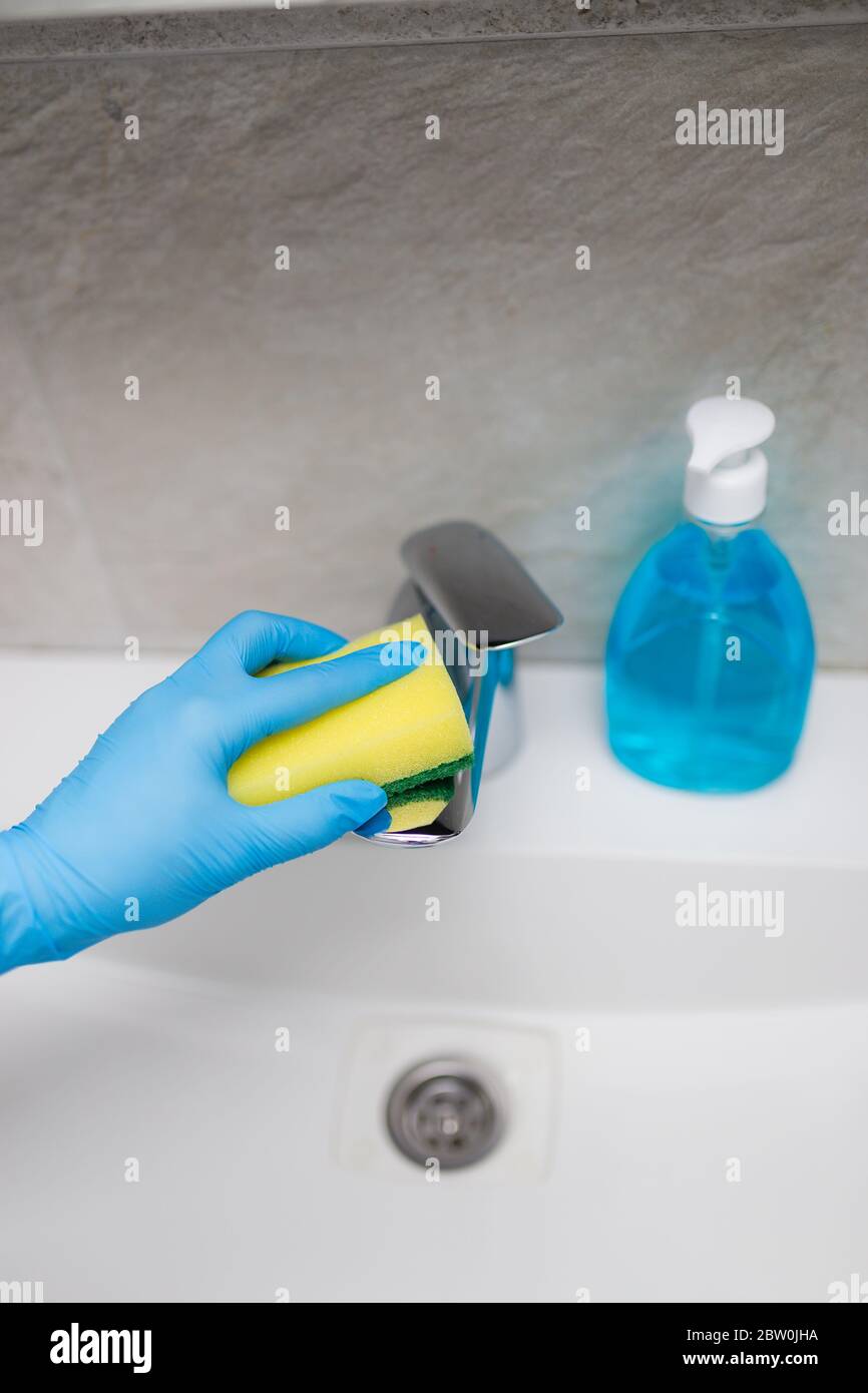 Female hand cleaning sink tap faucet in bathroom to disinfect from