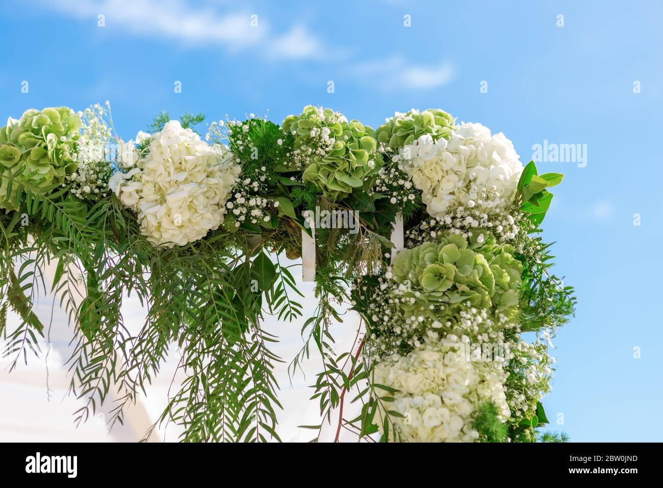 A wedding decorated with a luxurious arch of fresh flowers on a sunny day against a blue sky. Close-up. Stock Photo