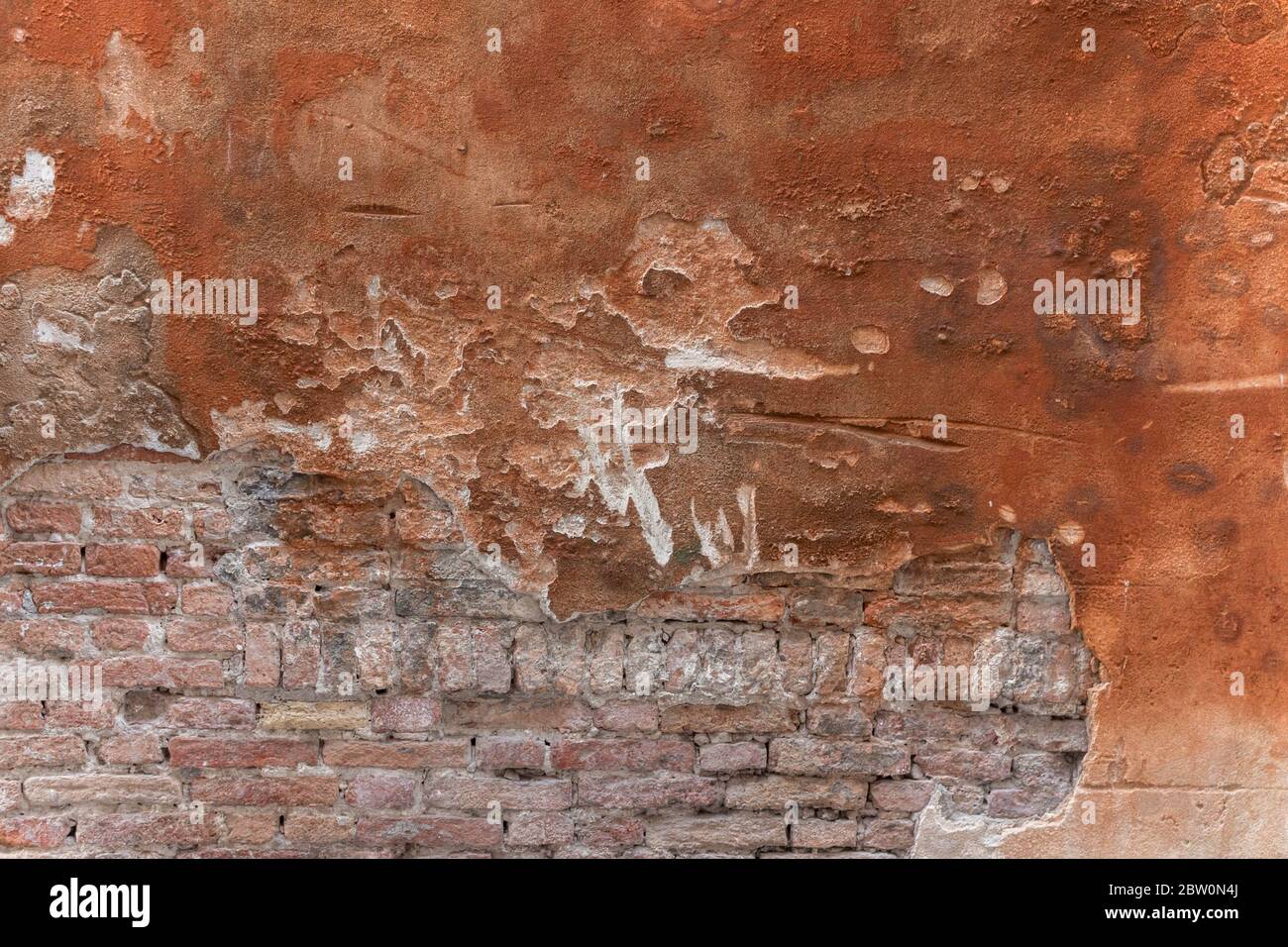 Unfinished red plastered wall with bricks showing through Stock Photo