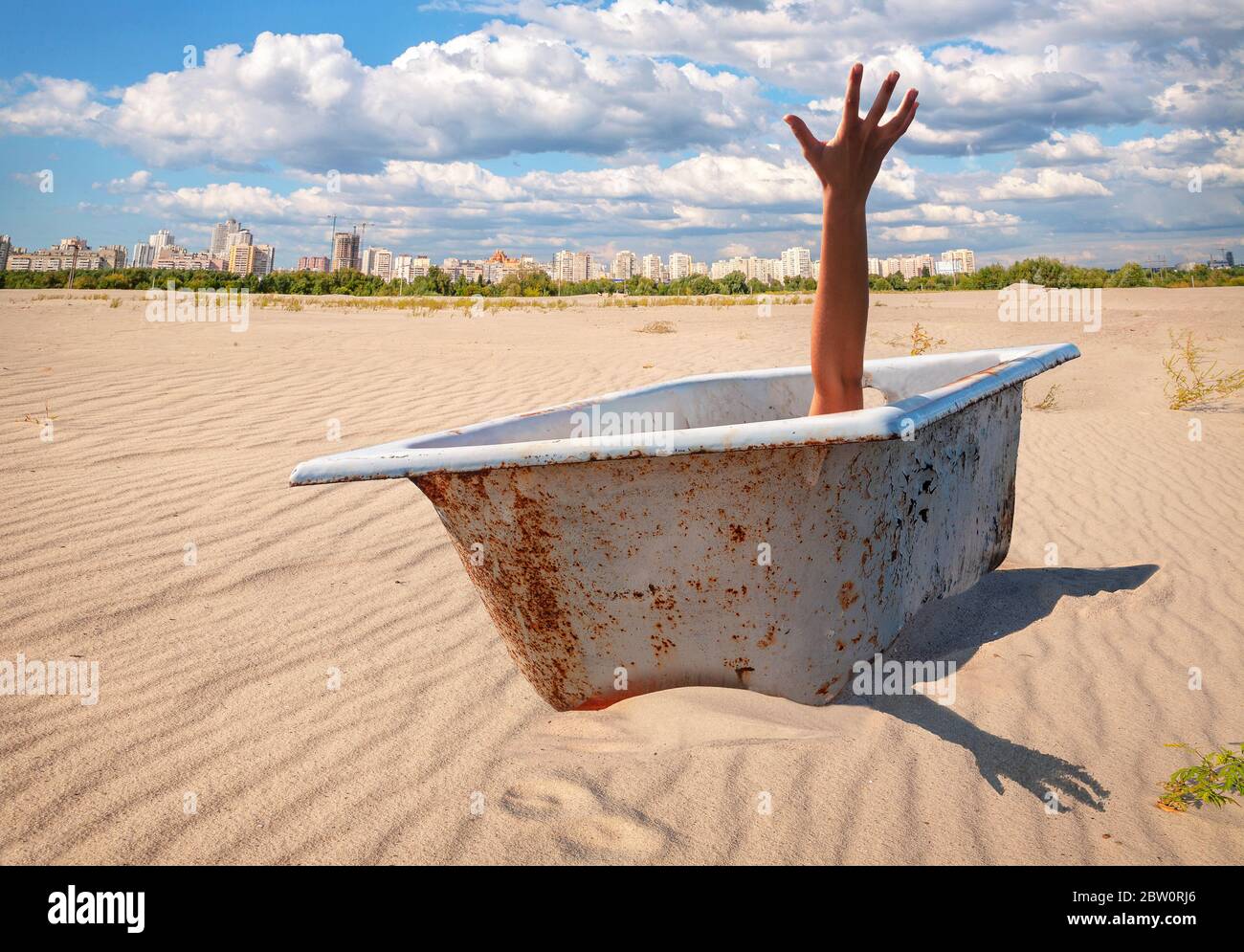 Obsolete cast iron bathtub with lifted to sky a hand in distancing outside city in desert sandy area.Concept of self isolation, quarantine Stock Photo
