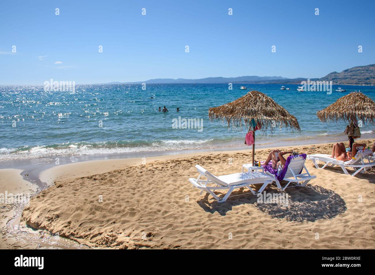Pefkos beach with holiday-makers, sun beds and umbrellas in village of Pefkos (Rhodes, Greece) Stock Photo