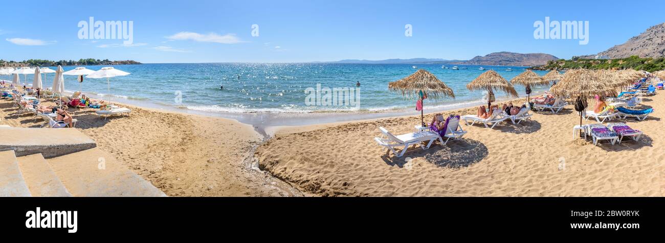 Pefkos beach with holiday-makers, sun beds and umbrellas in village of Pefkos - PANORAMA (Rhodes, Greece) Stock Photo