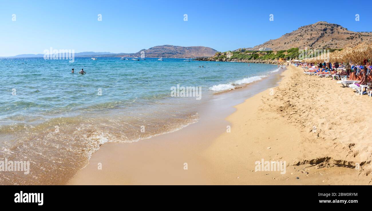 Pefkos beach with holiday-makers, sun beds and umbrellas in village of Pefkos - PANORAMA (Rhodes, Greece) Stock Photo
