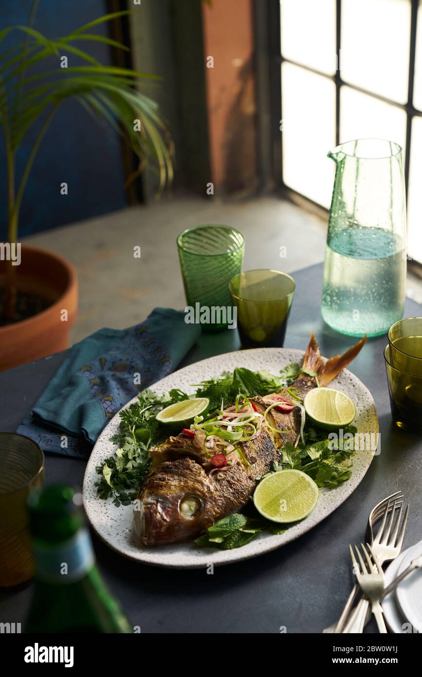 Roasted whole fish dish in a table setting with glasses and napkin