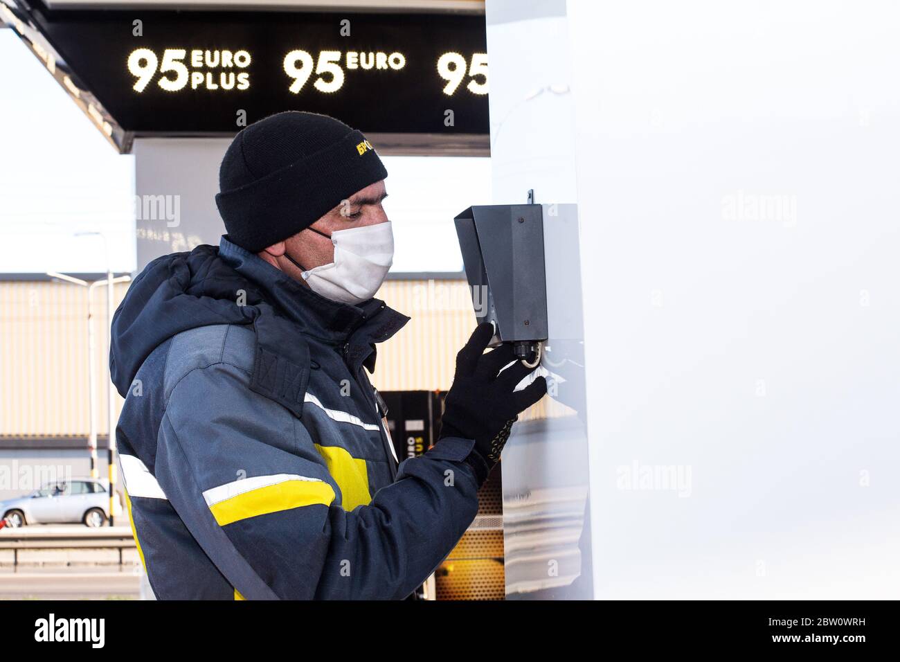 April 2020 during corona virus one of Kiev petrol stations operator in mask and gloves chats via speaker phone to help driver filling tank w fuel. Stock Photo