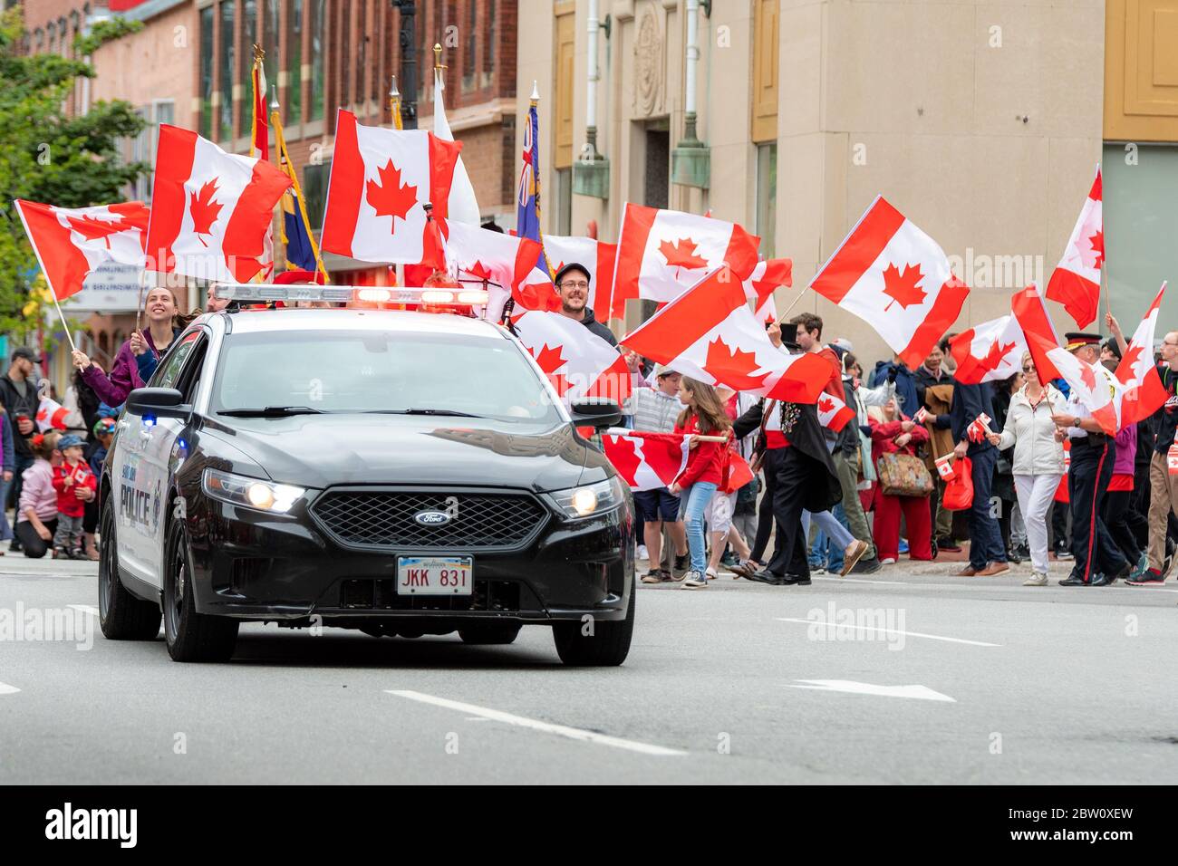 Saint John, New Brunswick, Canada - July 1, 2019: A police car leads the Canada Day parade. Many people with Canadian flags follow. Stock Photo