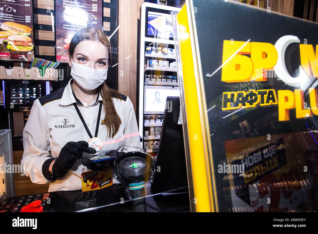 April 2020 during 1st lockdown at Kiev petrol station operator young woman in mask and gloves accepts driver's payment from behind plastic protection Stock Photo