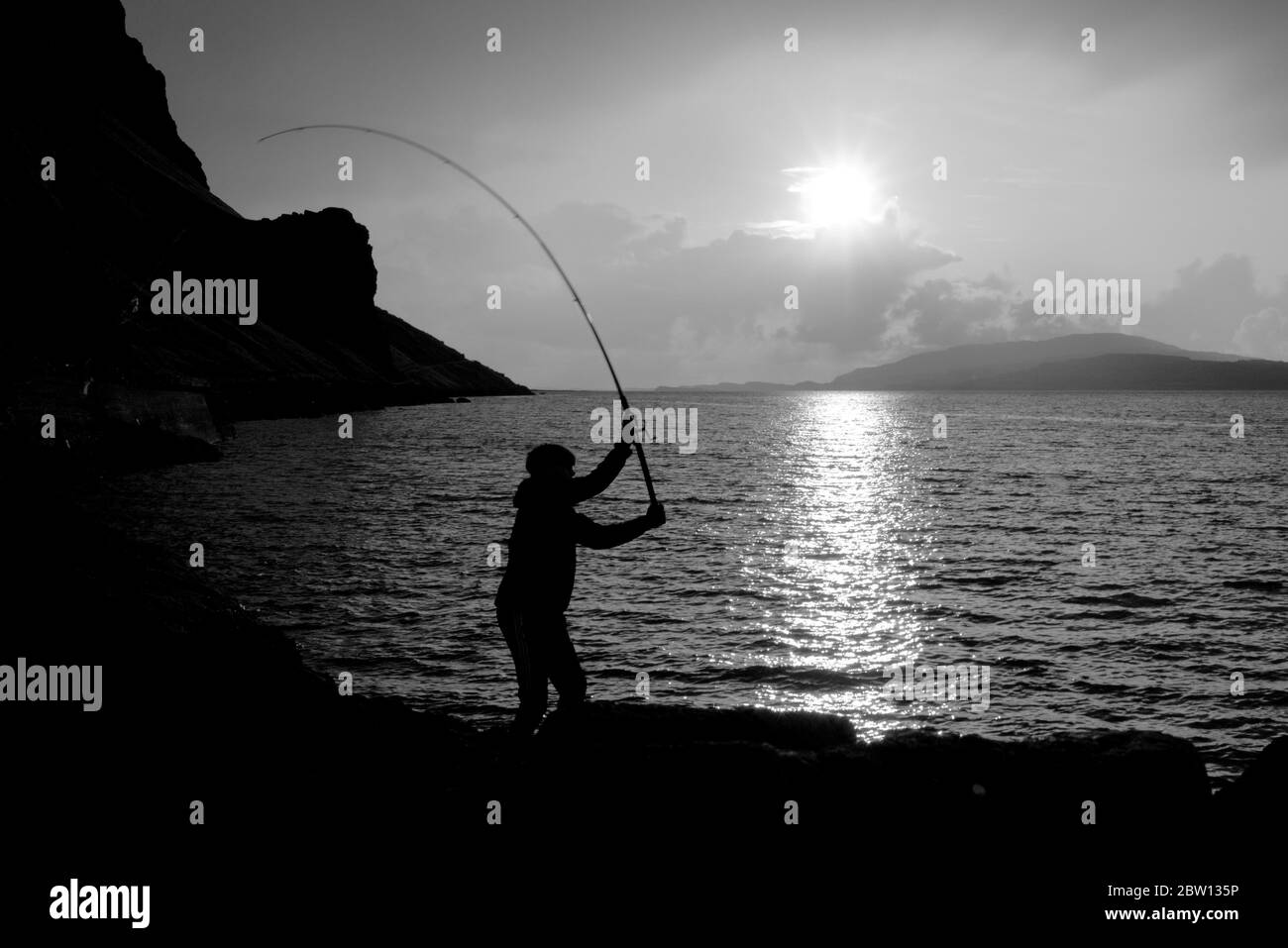 sunsets over loch na keal on the isle of mull as a young man fishes for mackerel in black and white Stock Photo