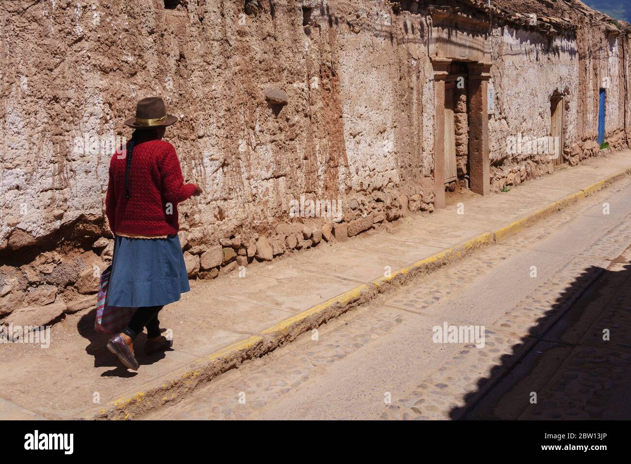 Quechuan woman walks along adobe walls of street in Moray in Sacred Valley of Peru. Stock Photo