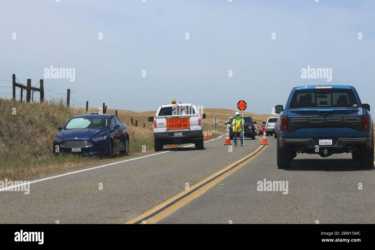 Road work on Hwy 120 grinds traffic to a halt.  A construction worker wearing a mask directs one lane traffic using a Stop and Slow sign. Stock Photo