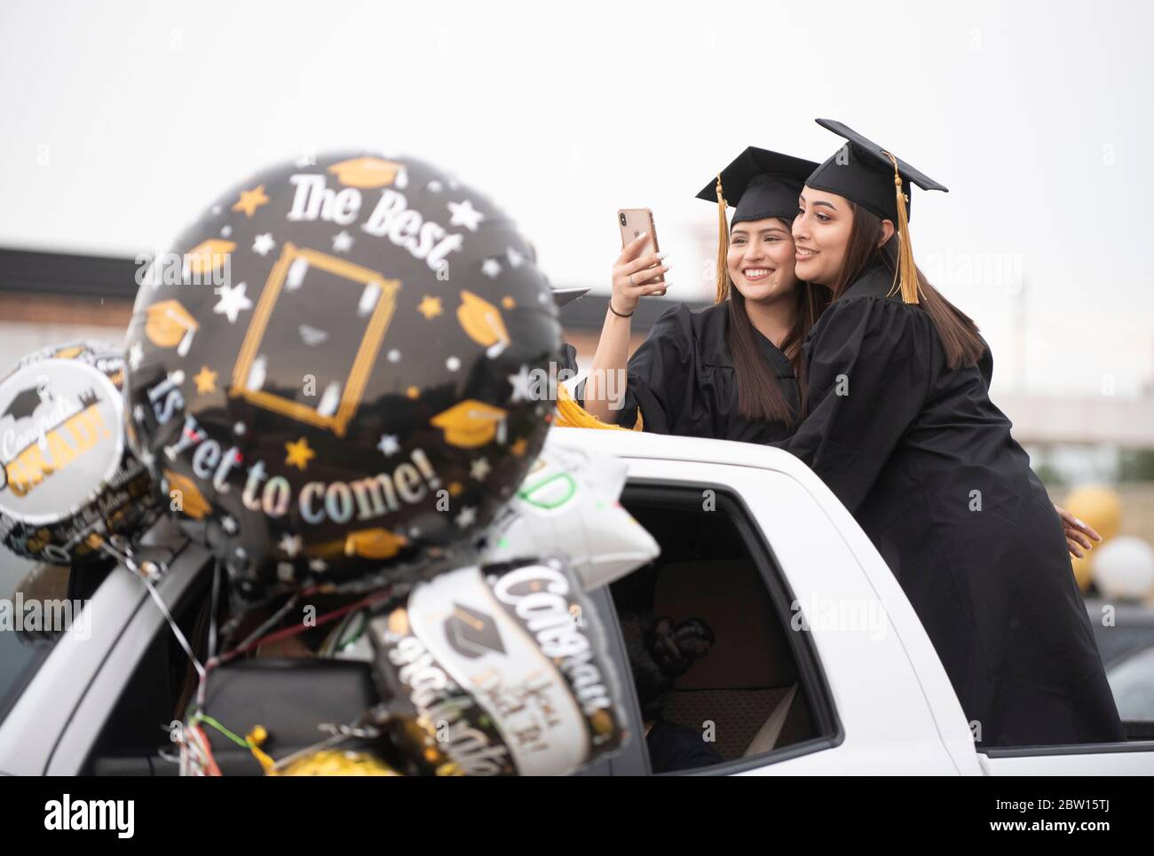 Graduates of Navarro Early College High School, including Esmerelda Alvarez (l) and Alma Pina, parade through their north Austin neighborhood on May 28, 2020 as they celebrate an academic finale shortened by the coronavirus pandemic. About 200 graduates piled into cars, waving at family and friends in the two-mile parade. Credit: Bob Daemmrich/Alamy Live News Stock Photo