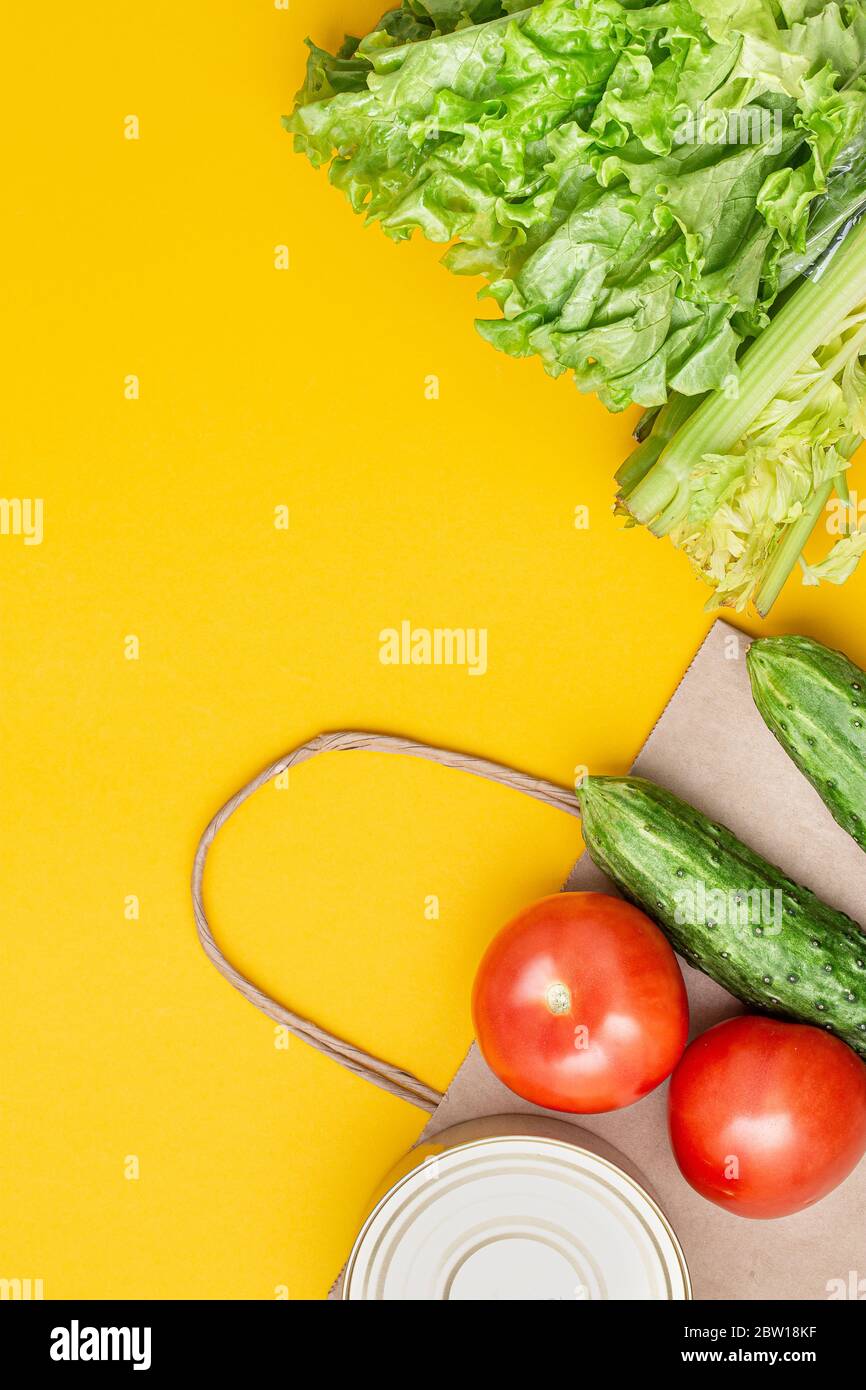 Paper bag with food, canned food, tomatoes, cucumbers, bananas, lettuce on a yellow background. Donation, coronavirus quarantine. Food supplies for qu Stock Photo