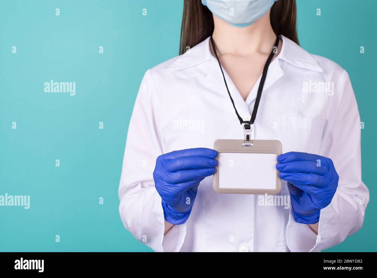 Close-up cropped photo of female doctor in white coat hazard uniform gloves holding a blank maok up nametag isolated on blue background Stock Photo
