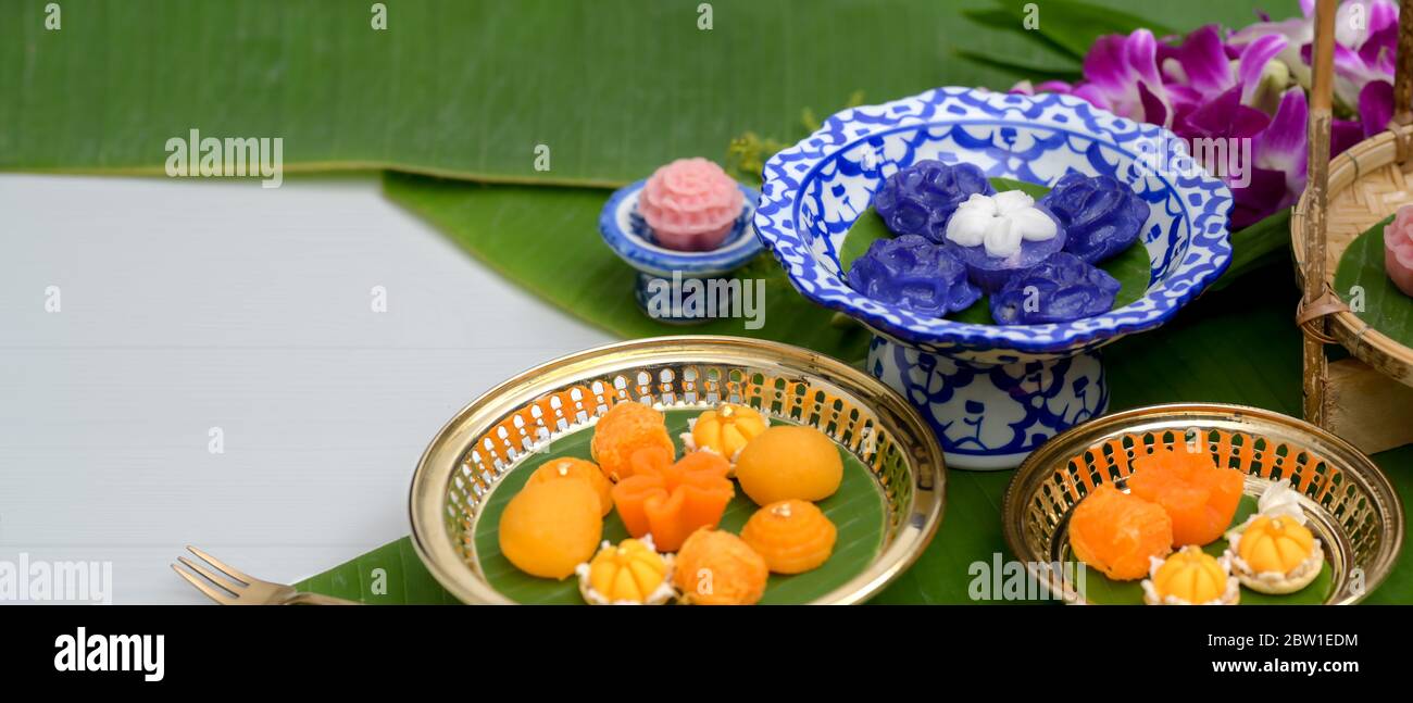 Close up view of several Thai traditional dessert serving on porcelain and brass tray with flower and banana leaves decorated on white table Stock Photo
