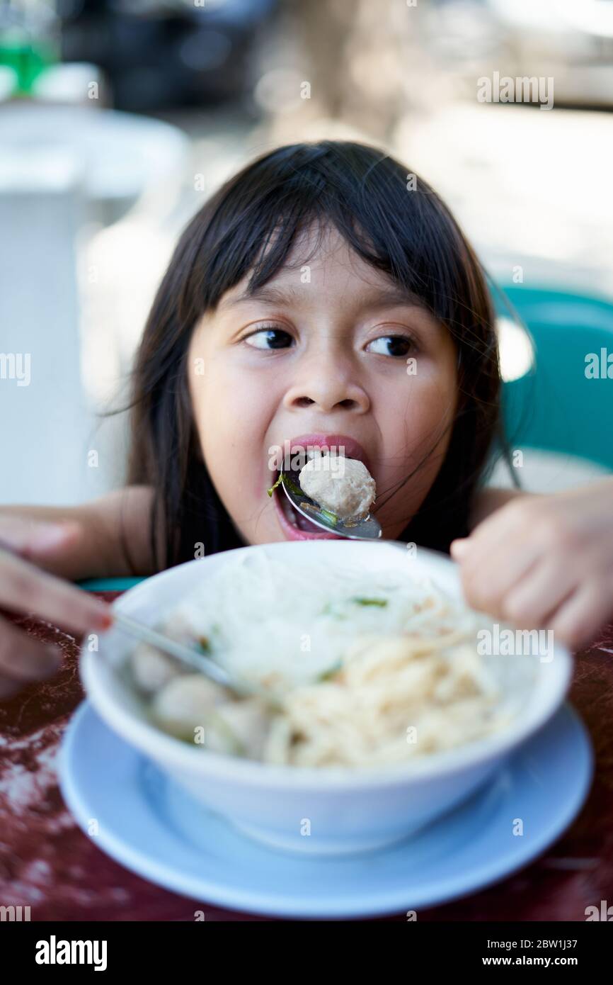 Little asian girl eating ramen noodles soup with meatballs at street food market Stock Photo Alamy