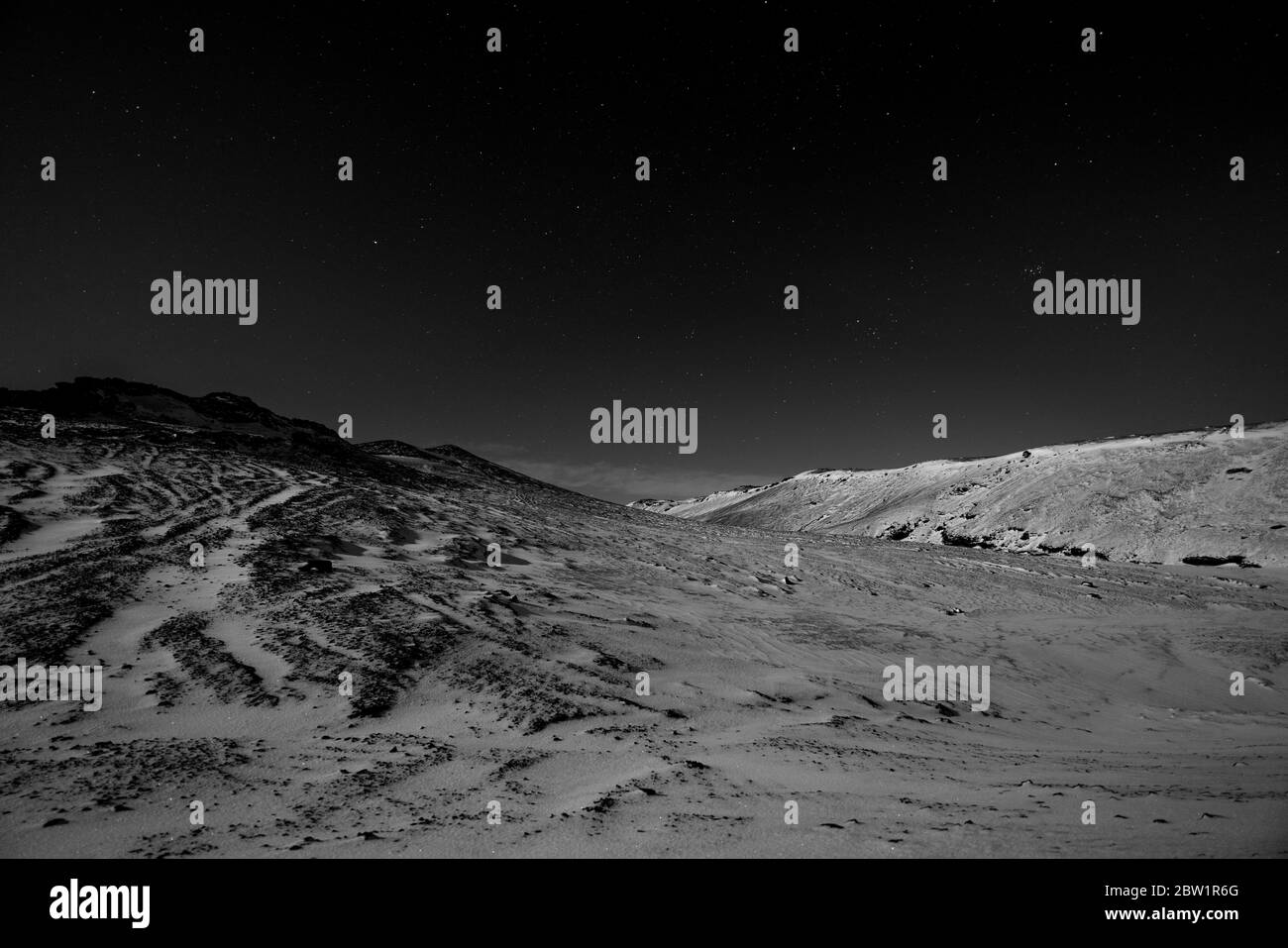 Black and white photo of a snow covered landscape in moonlight with a starry dark sky. Stock Photo