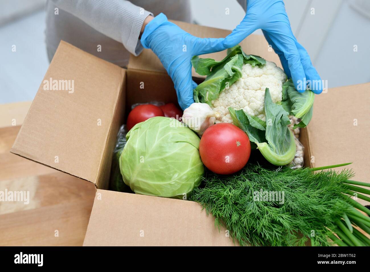 Volunteer in gloves with food donation box puts vegetables to help others. donation box with foodstuffs Stock Photo