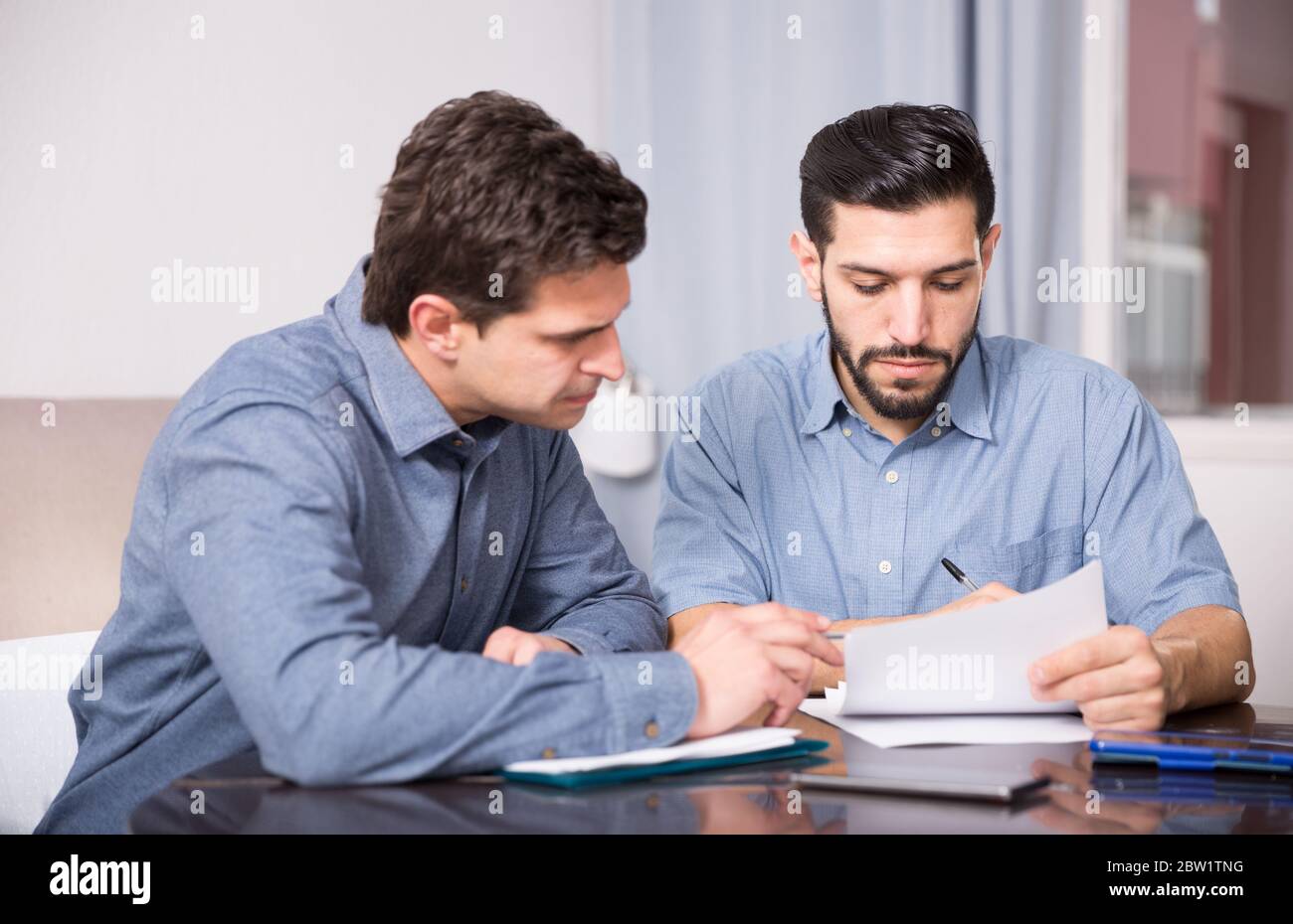 Two young men in serious discussion at home table while analysing documents together Stock Photo