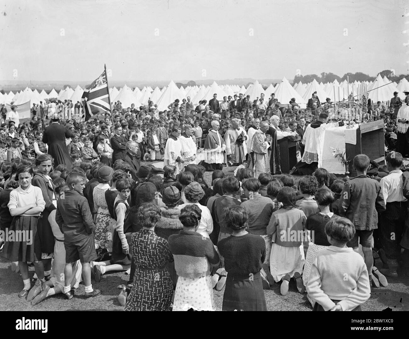 Basque children in religious procession has Hampshire camp. Led by the 15 priests who accompanied them from Spain, the refugee Basque children marched in procession around the North Storeham camp near Southampton, to celebrate the Feast of Corpus Christi. Banners and other equipment was sent from the neighbourhood. Photo shows, a general view of the service at the refugee camp. 27 May 1937 Stock Photo