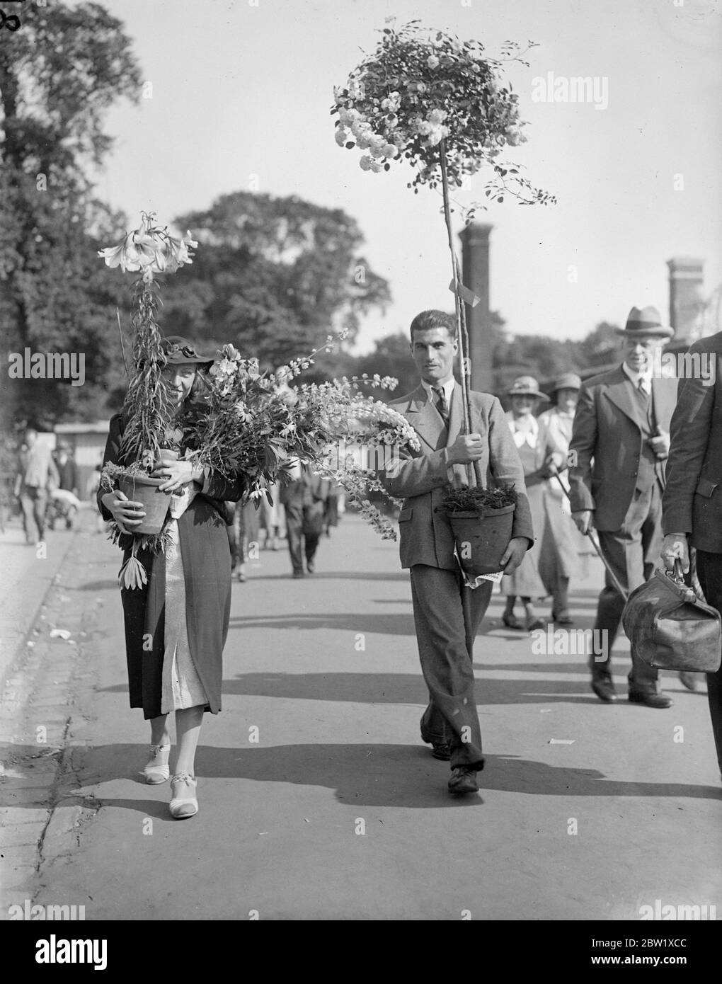Harvest of the Chelsea flower show. Hundreds of blooms were given away at the Royal Hospital grounds when the Chelsea flower show came to an end today (Friday). Photo shows people leaving the flower show laden with blooms after the show had closed. 28 May 1937 Stock Photo