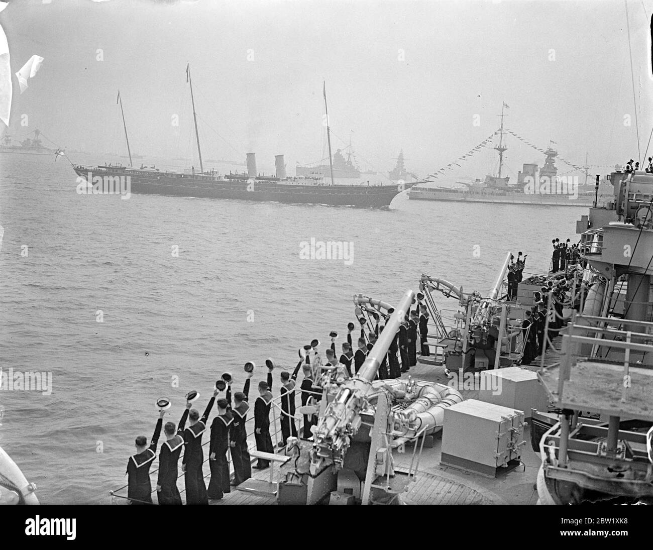 The King reviews fleet at Spithead. Aboard the Royal yacht, 'Victoria and Albert', the King passed through the 5 mile line of 160 warships and merchant vessels when he made his Coronation review of the British Navy and Mercantile Marine at Spithead. Nearly 300 ships, including 17 from the foreign fleets, were reviewed. Photo shows, men of 'HMS London (P 69 ) cheering the Royal yacht 'Victoria and Albert' as she passed down the lines with the King aboard. 20 May 1937 Stock Photo