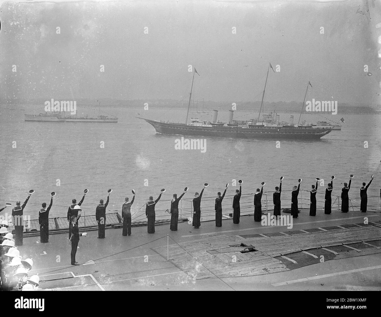The King reviews fleet at Spithead. Aboard the Royal yacht, 'Victoria and Albert', the King passed through the 5 mile line of 160 warships and merchant vessels when he made his Coronation review of the British Navy and Mercantile Marine at Spithead. Nearly 300 ships, including 17 from the foreign fleets, were reviewed. Photo shows, men of the aircraft carrier HMS Glorious cheering as the Royal yacht 'Victoria and Albert' passed down the lines with the King aboard. 20 May 1937 Stock Photo
