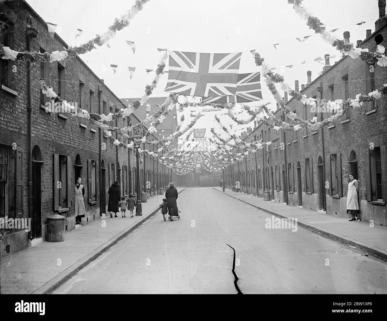 East End surpasses itself for Coronation. Gathering funds by door-to-door collections, many of the poorest streets in the East End of London have rivalled the West End with the brilliance and variety of their decorations for the Coronation. Photo shows: Bunting and flags slung from house to house from the Coronation decoration scheme of Appleby Street, Shoreditch. 7 May 1937 Stock Photo