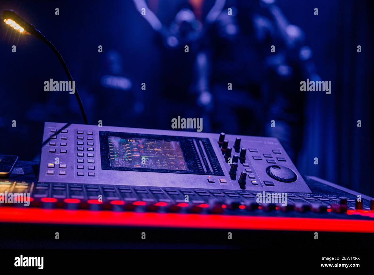 An advanced mixing console in dim coloured lighting, with the stage posing  in the background Stock Photo - Alamy