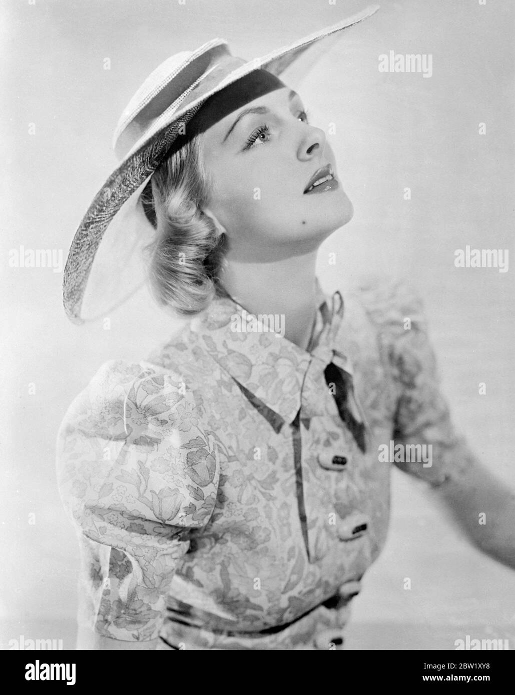 Film actress as own hat designer. Photo shows: Miss Orien Hayward, Hollywood film actress, wearing a becoming natural coloured straw hat which she designed herself. The hat has bands of brown grossgrain. With its she wears a washable summer dress of printed linen in yellow, blue and apple green. 7 May 1937 Stock Photo