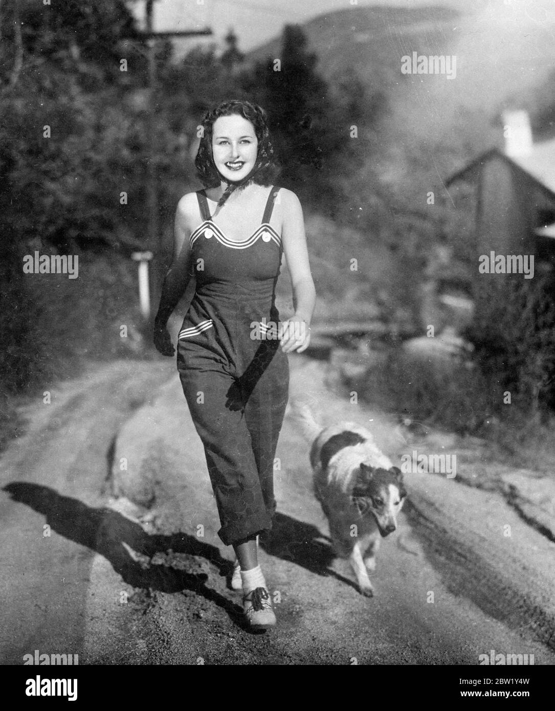 Overalls as film actress walking costume. Barbara Read, the film actress, prefers comfort when walking, exercising her dog between 'shots' of her new film Make Way for Tomorrow. Her inexpensive, but attractive overalls of the blue, set off by white striping at the neckline and pockets. Stock Photo