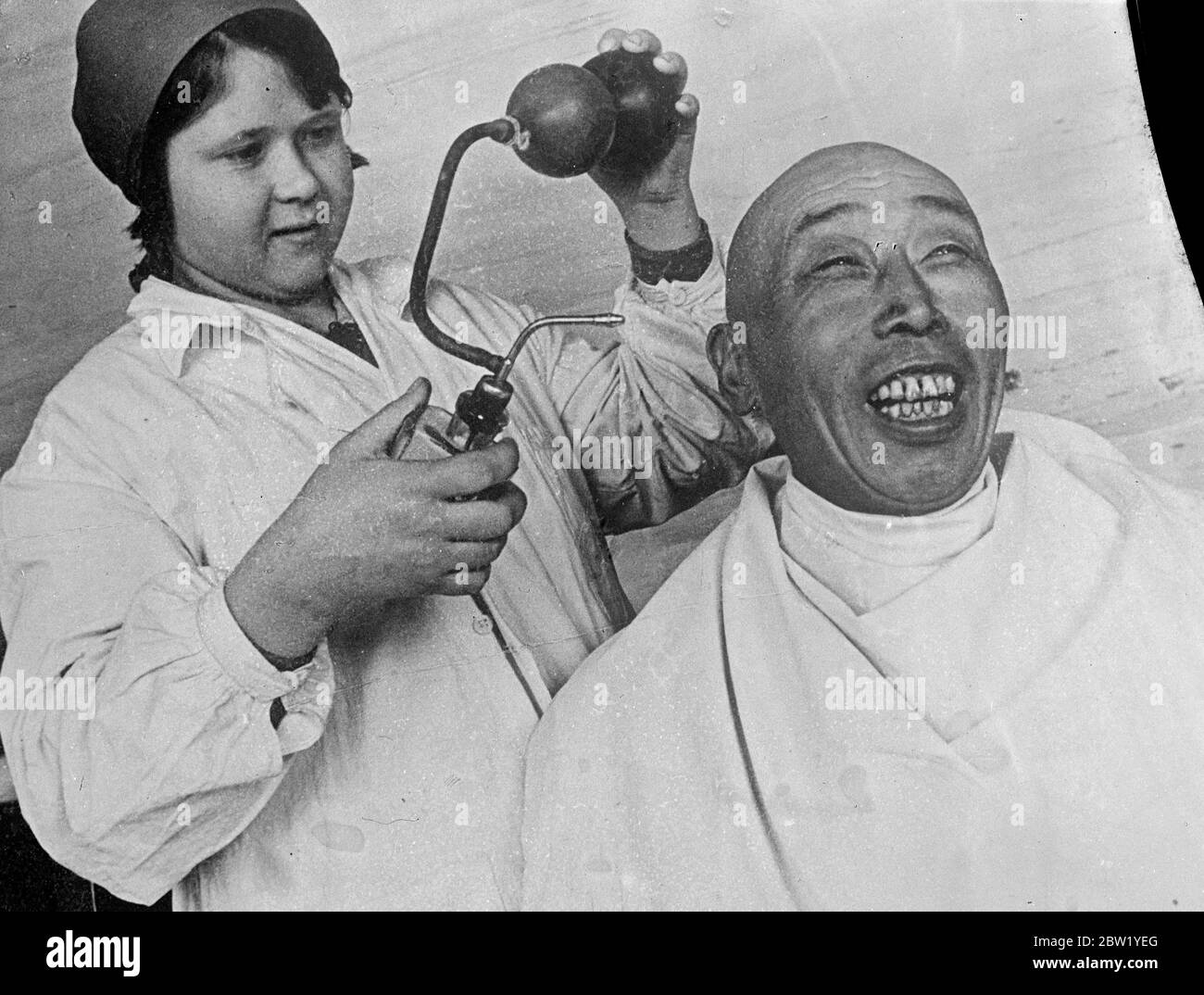 Original caption: He likes the spray! Oriental impassiveness gave place to a broad smile of delight as the woman barber scent sprayed her Chinese customer in a shop at the Svetly gold field in the Lena River district of Eastern Siberia, USSR. This miner is one of the many Chinese working in the Lena goldfields. Stock Photo
