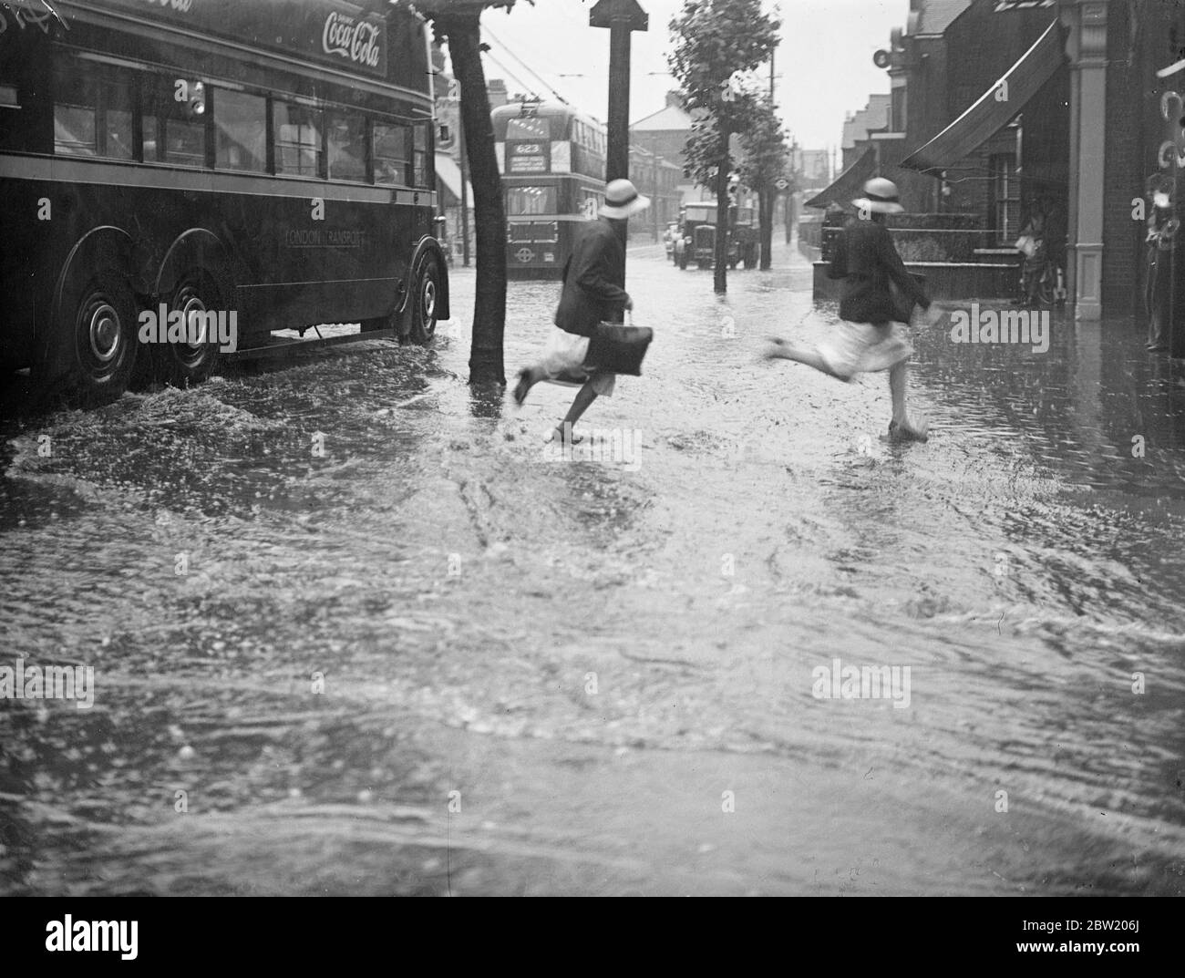 Schoolchildren running through the floods at the junction of Forest Road and Chingford Road Walthamstow. Torrential rains and flooded roads followed a terrific summer thunderstorm which created havoc in Walthamstow. The manholes in Walthamstow and Chingford district were forced up by the floods.. 15 July 1937. Stock Photo