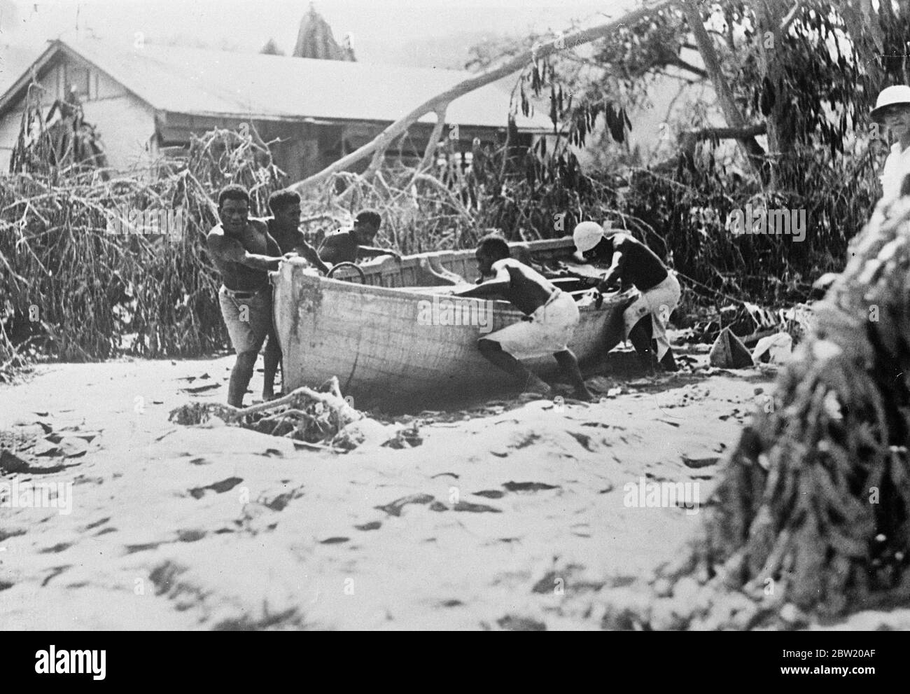 First pictures of volcano disaster on New Guinea island. Three volcanoes, 2 on Vulcan Island and one on the Matupi Island, erupted violently showering pumice and mud on the roofs of Rabaul chief town of New Britain Island in New Guinea. Photo shows: Natives at Rabaul removing boat which was carried 300 yards inshore by tidal wave [tsunami]; broken trees in the background. 18 June 1937 Stock Photo