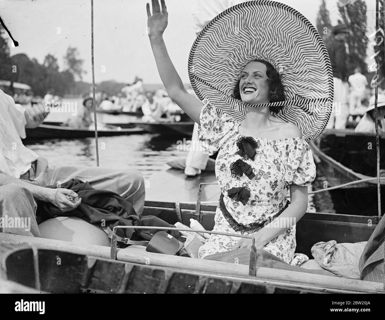 With the heatwave as encouragement, Henley's Royal Regatta vied with Ascot in variety of its fashion. An enormous hat fashion, the largest seen on the river worn by a spectator who cheered her crew to victory from a punt along the boom during the final day's racing at Henley. 3 July 1937 Stock Photo