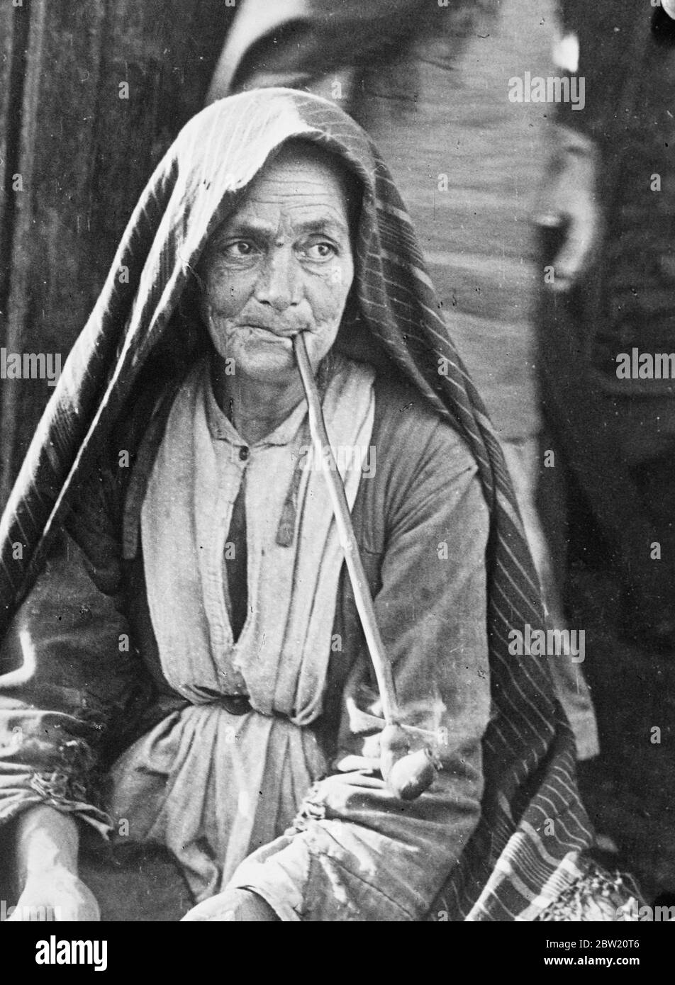 Elderly Jewish woman pipe addict of a Russian ghetto dressed in coarse cloths and shawl. She is contentedly smoking her long pipe, rudely made from wood, in the ghetto of Derbent / Derbend, Dagestan Republic on the shores of the Caspian Sea USSR. 9 July 1937 Stock Photo
