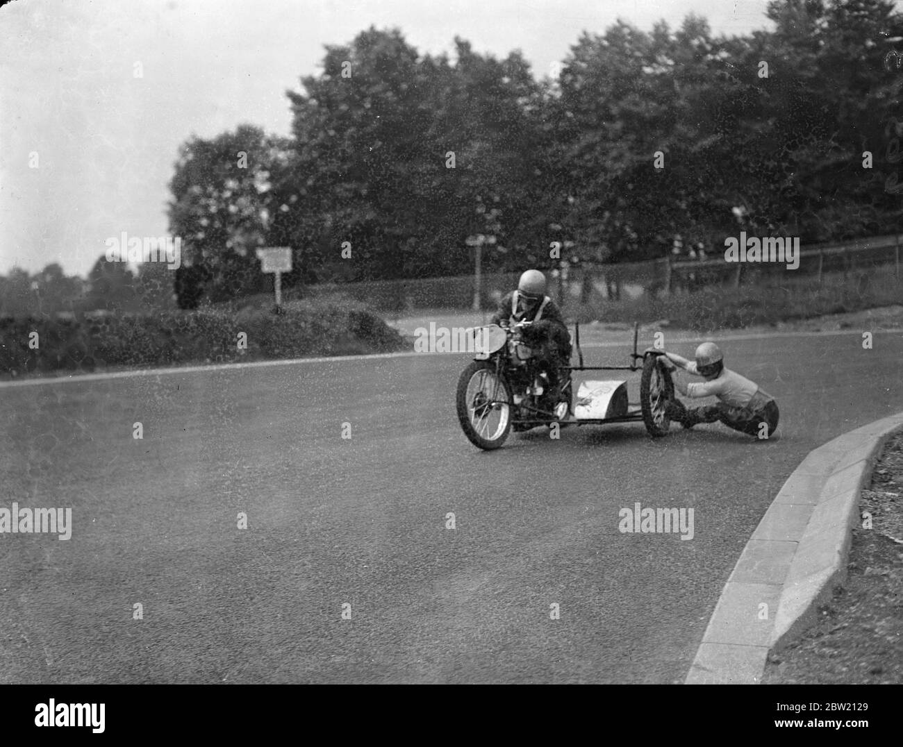 Motor cyclists had a final practice on the Crystal Palace Road Racing Circuit for the London Grand Prix meeting today (Saturday). The passenger nearly on the ground as he clings to a wheel when John Surtees rounds New Zealand Bend. 17 July 1937. Stock Photo