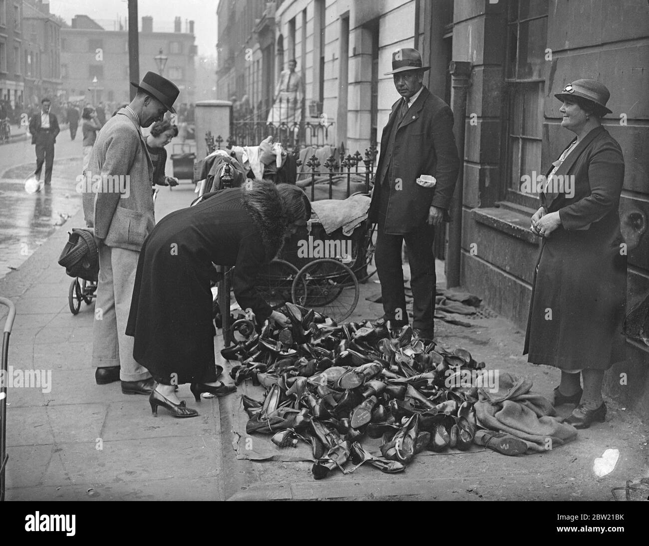 A woman shopper selecting a pair of shoes from a pile on the pavement of the Rag Market, Notting Hill, London's famous street market, which is threatened with extinction. A petition with 5000 signatures is being organised for presentation to Parliament in an attempt to save the market. 29 August 1937 Stock Photo