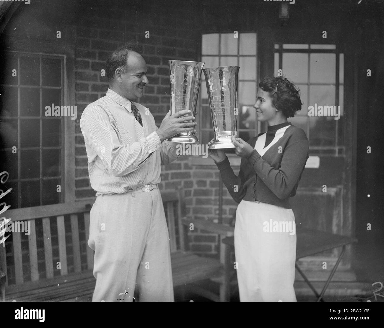 Monsieur A.M Vagliano and Mlle. Lally Vagliano, exchange toasts with their cup after wiining the annual Fathers and Daughters golf match by defeating Mr J.S Ruttle and Miss M. Ruttle by 3 and 2 at the West Sussex Club. 3 September 1937. Stock Photo