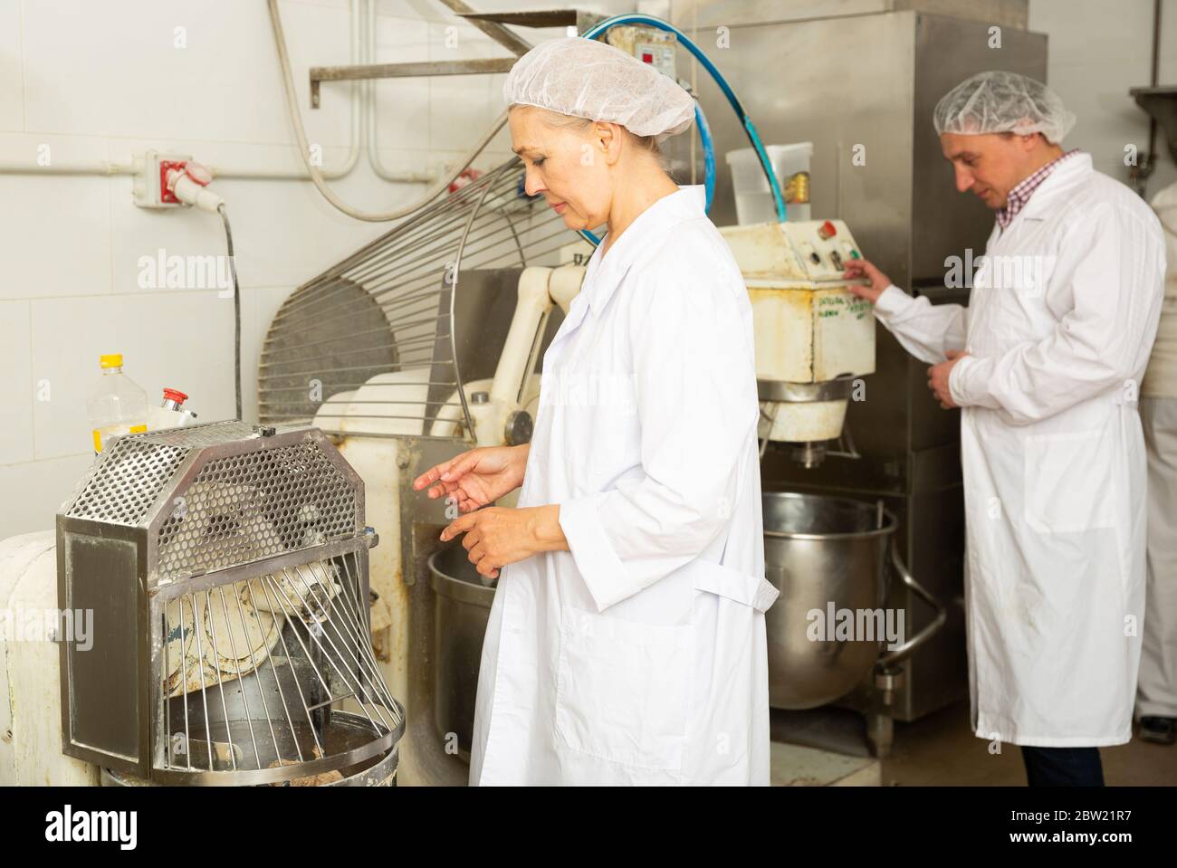 Portrait of two experienced bakery workers watching work of kneading machine making dough Stock Photo
